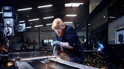 Ein Mann sägt an einem Metallteil, das auf zwei Metallträger gespannt ist