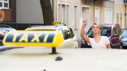 Person mit blonden geschlossenen Haaren hebt die Hand und ruft ein Taxi