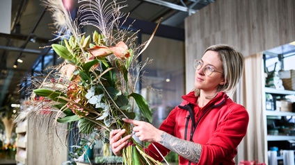 Eine junge Frau bindet einen Strauß Blumen zu einem Gesteck in einer Gärtnerei