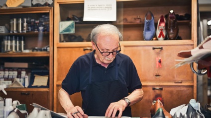 Ein Schuhmacher arbeitet in seiner Werkstatt an einem Tisch und bereitet Material vor