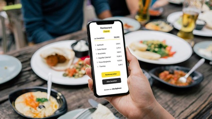 Handy mit der App im Einsatz vor dem Hintergrund eines mit Speisen und Getränken gefüllten Tisches in einem Restaurant