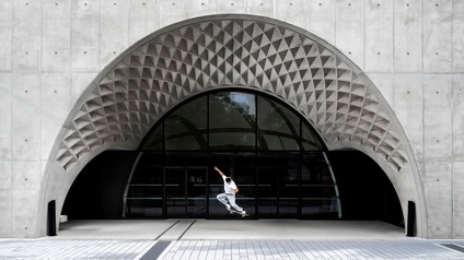 Mann auf einem Skateboard in der Luft, im Hintergrund sieht man ein Gebäude