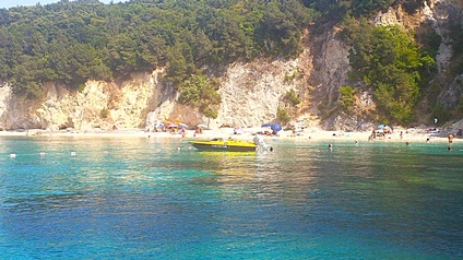 Ein Motorboot im türkisen Wasser vor einer mit Bäumen überwachsenen Steilküste