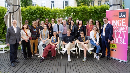 Gruppenbild einer Netzwerkveranstaltung, die Teilnehmer stehen im Freien. In der rechten Bildhälfte ist ein Roll-up mit der Aufschrift Junge Wirtschaft setzt Impulse