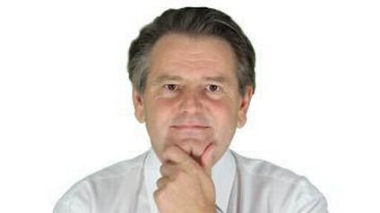 Mann mit weißem Hemd und grauen Haaren hält linke Hand an Kinn