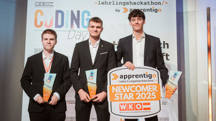 Die drei Sieger beim Bundeslehrlingshackathon 2025 in schwarzen Anzügen halten ihre Trophäen und ein Schild mit der Aufschrift Newcomer Star 2025