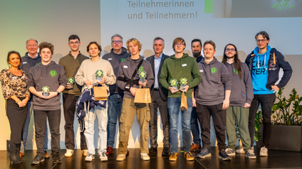 Gruppenfoto von Männern, Frauen und Jugendlichen auf einer Bühne - die Jugendlichen präsentieren kleine Trophäen