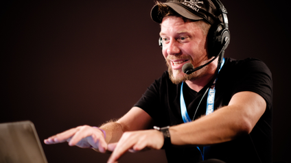 Mann mit Headset und Schilkappe mit der Aufschrift St. Pauli streckt seine Hände aus in Richtung eines Laptops