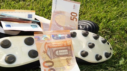 Fußballschuhe und Euroscheine liegen am Rasen.