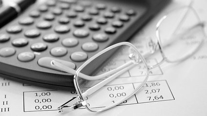 Detailansicht Brille neben Taschenrechner auf Papier mit Zahlen liegend