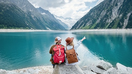 Zwei Wanderer sitzen am Seeufer, Berge im Hintergrund