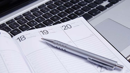 Detailansicht eines Kalenders, daraufliegend Kugelschreiber, im Hintergrund Computertastatur