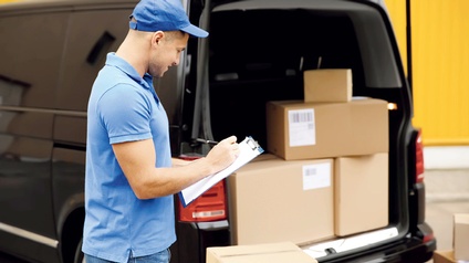 Ein blau gekleideter Mann mit Klemmbrett vor seinem schwarzen Kleintransporter, gefüllt mit Paketen.