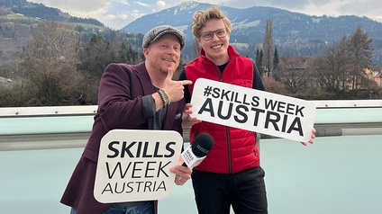 Zwei Personen stehen vor Berglandschaftt mit Schildern mit Schriftzug Skills Week Austria in Händen
