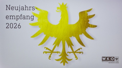 Auf einer Projektionsfläche ist ein goldener Tiroler Adler vor hellem Hintergrund zu sehen. Links daneben steht der Text „Neujahrsempfang 2026“. Rechts unten befindet sich das Logo der Wirtschaftskammer Tirol, Bezirksstelle Schwaz. Das Bild wirkt feierlich und repräsentativ.