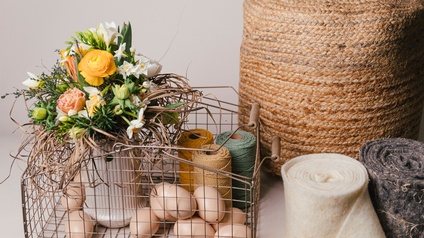 Blumenstrauß in einer Vase gemeinsam mit Eiern und bunten Zwirnen in einem Korb 
