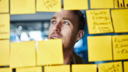 Person lugt durch transparente Wand voll beklebt mit gelben Post-its