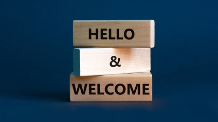 Drei Holzblöcke mit Schriftzug Hello and Welcome vor einem dunkelblauem Hintergrund