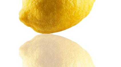 Vor weißem Hintergrund ist eine gelbe Zitrone mit einem Blatt, die sich spiegelt