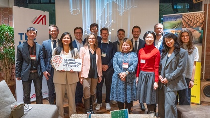 Gruppenfoto von mehreren Personen in Bürokleidung vor einer Leinwand, auf der die Karte Europas projiziert ist. Eine der Personen hält ein Schild, auf dem global incubator network steht