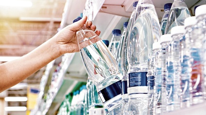 Eine Hand greift im Supermarkt nach einer Wasserflasche, die neben vielen anderen in einem Regal steht