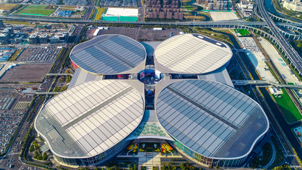 Aufnahme einer großen Halle aus der Vogelperspektive mit vier Gebäudeteilen. Um das Gebäude sind mehrere Parkplätze