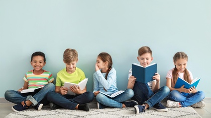 Fünf Kinder sitzen in einer Reihe im Schneidersitz und lesen Bücher