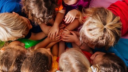 Kinder spielen gemeinsam auf einer bunten Decke und halten die Hände zusammen, Topview