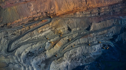 Aufnahme eines Bergwerks aus der Luft mit verschlungenen Wegen, die vom Rand des Werks nach unten führen. Auf den Wegen fahren mehrere Fahrzeuge