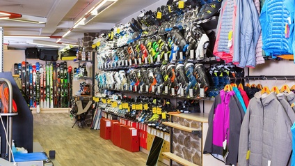 Sportfachgeschäft mit Regal voller Schischuhe, nebenbei Jacken hängend