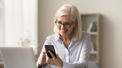 Ältere Frau beim Arbeiten mit Handy und Laptop