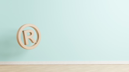 Grafik des Großbuchstabens R, der von einem Kreis umrahmt wird und über einen Holzfußboden schwebt vor einer hellblauen Wand