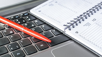 Detailansicht eines roten Kugelschreibers auf Tastatur liegend, daneben Kalender platziert