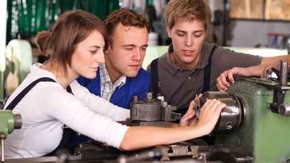 Drei Personen blicken auf Maschine, eine der Personen hält Messzange an die Maschine.