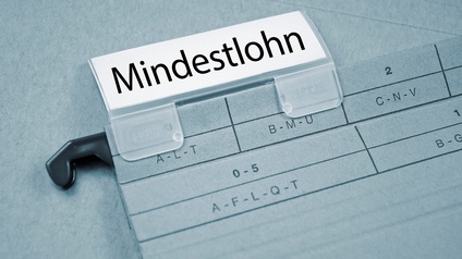 Nahaufnahme eines Ordners zum Aufhängen, worauf ein Plastikschieber befestigt ist. Darin befindet sich ein Stück Papier, bedruckt mit dem Wort Mindestlohn