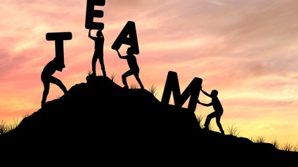Konzept Team-Work mit Buchstaben, die auf einen Hügel von Personen gemeinsam getragen werden, im Hintergrund zeigt sich eine Abendstimmung