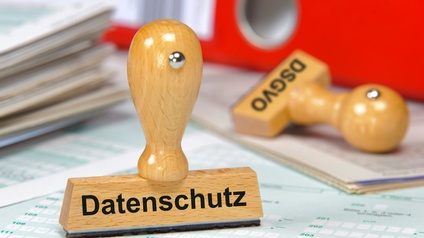 Stempel mit Schriftzug Datenschutz steht auf Formularen, dahinter liegt ein weiterer Stempel mit Aufschrift DSGVO
