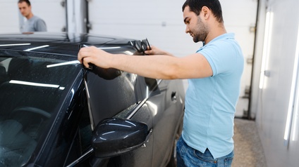 Person steht neben Auto und appliziert Folie auf Autofenster des Fahrersitzes