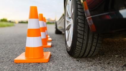 Nahaufnahme dreier nebeneinander stehender Verkehrshütchen, die neben einem PKW stehen