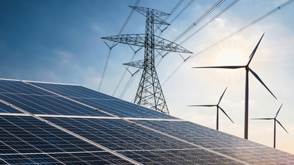 Im Vordergrund sind Solaranlagen, daneben stehen ein Strommast und Windräder.