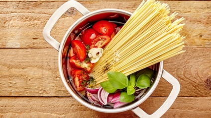 Frisches geschnittenes Gemüe, Kräuter und Spaphetti in einem Topf für Zubereitung von Pasta auf Holzuntergrund
