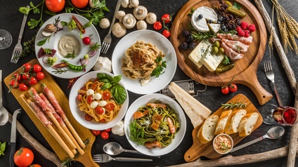 Verschiedene Pastagerichte, Käse, Prosciutto, Baguette, Tomaten, Champignons, Kräuter, Himbeeren, Brombeeren, Parmesan auf Tellern und Holzbrettern