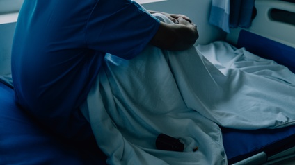 Aufnahme einer Person, die mit angewinkelten Beinen in einem Krankenhausbett sitzt