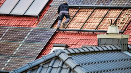 Person in Rückenansicht auf Dach gelehnt bei der Montage von Solarpanelen