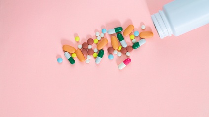 Verschiedenfarbige und -förmige Pillen neben liegender weißer Plastikflasche auf rosa Hintergrund