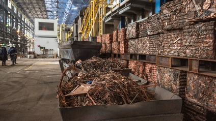 Kupferschrott in einem Container bereit für Recycling in einer Fabrikhalle, im Hintergrund stehen drei Personen in Schutzbekleidungen