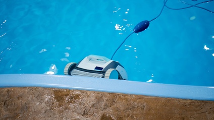 Ein automatisches Reinigungsgerät mit einem langen Kabel fährt die Innenwand eines Schwimmbades entlang