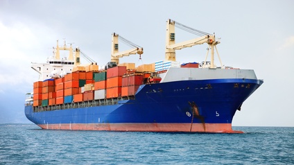 Großes blaues Transportschiff mit gelbbeigen Kränen am Deck beladen mit zahlreichen Frachtcontainern auf offenem Gewässer fahrend