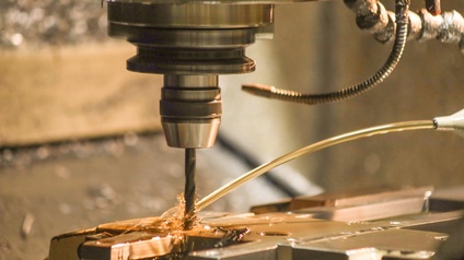 Automatisierung, ein Bohrer bohrt automatisch ein Loch in eine metallene Oberfläche, die gleichzeitig von der Seite mit einer geblichen Flüssigkeit bestrahlt wird