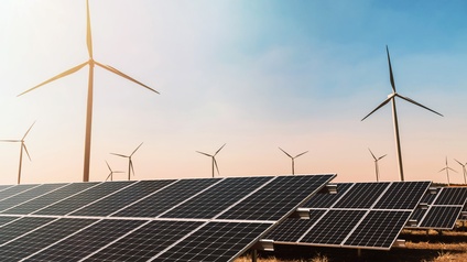 Feld im Sonnenuntergang: Im Vordergrund Solarpaneele, im Hintergrund Windräder